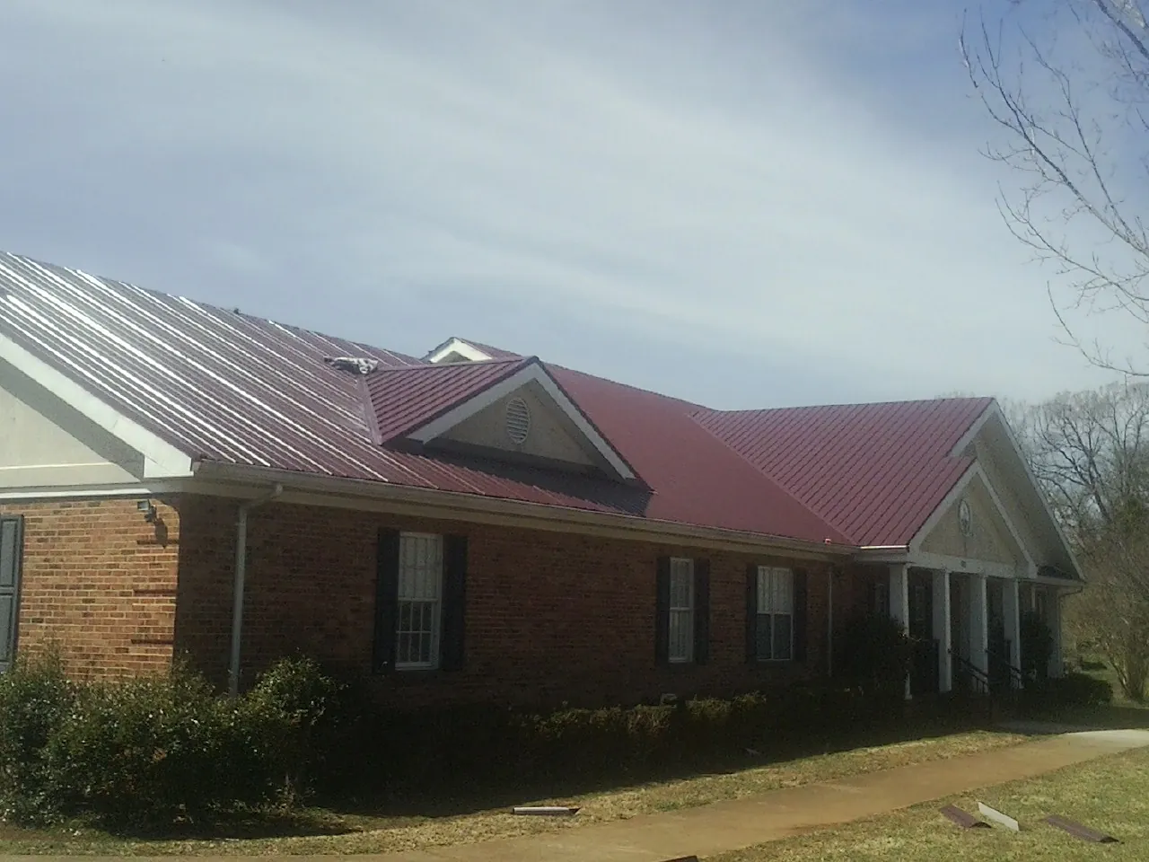 Red metal roof with gabled entries on a long brick building, from a Hail Damage Roof Repair job in Worthington